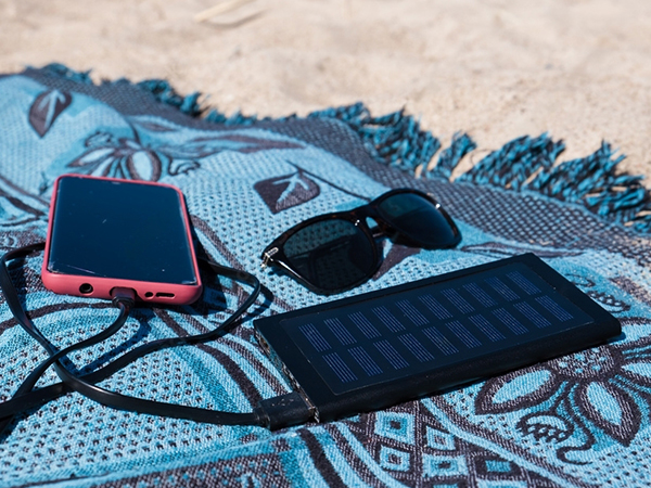 Un chargeur solaire portable est posé sur le sable, il est branché à un téléphone pour recharger la batterie.